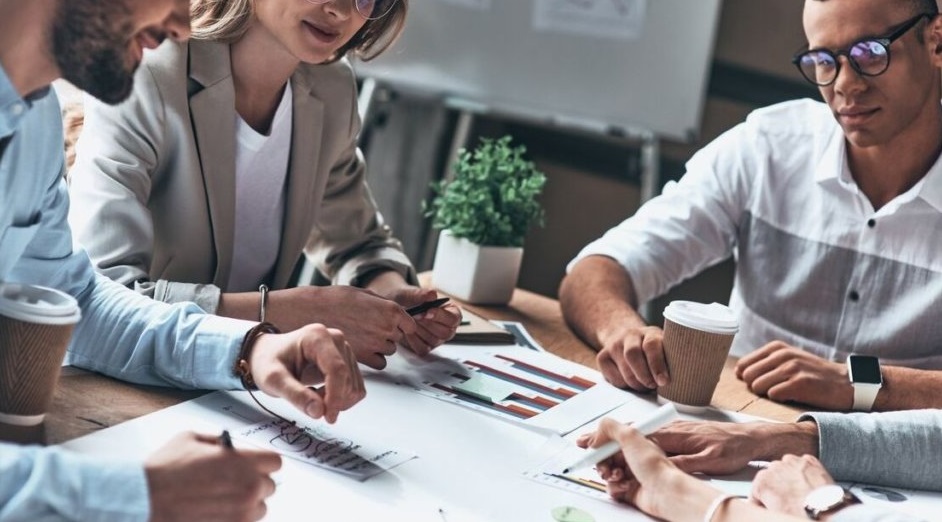 Employees have a discussion while sitting at a table with papers.